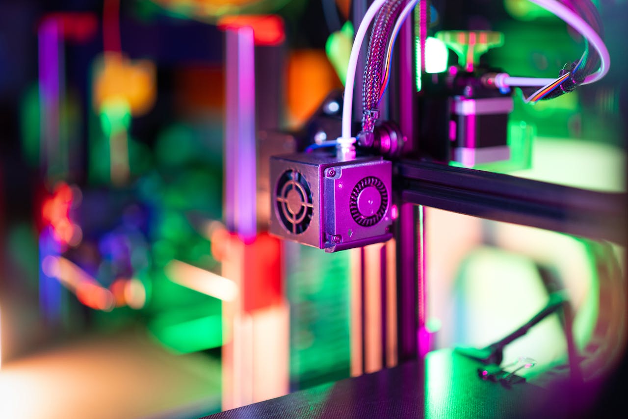 services-01 Vibrant neon-lit 3D printer in a modern workshop setting, showcasing advanced technology.